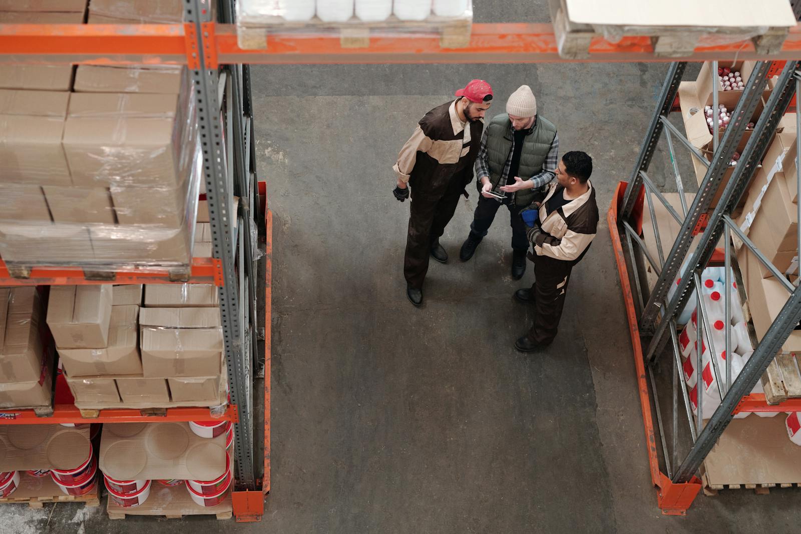 Three warehouse workers discussing logistics in an industrial storage area, bonds